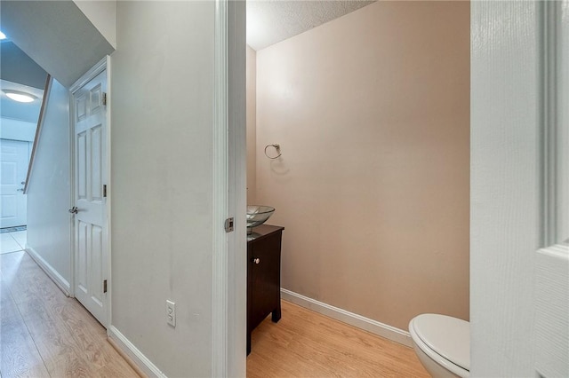 half bathroom with toilet, baseboards, wood finished floors, and vanity