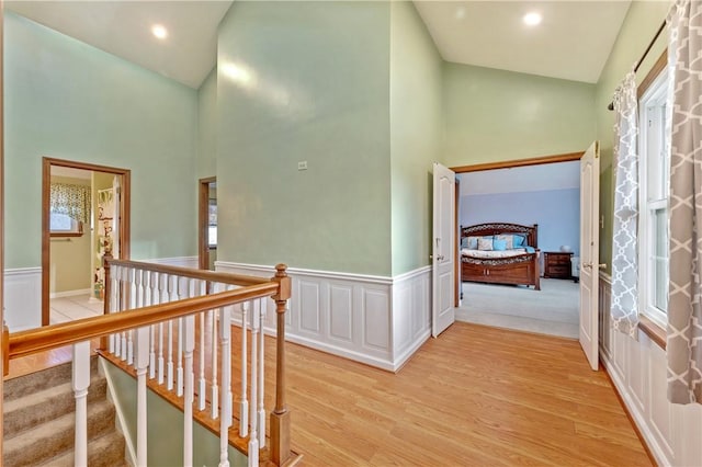 hall featuring light wood-style floors, recessed lighting, high vaulted ceiling, and wainscoting