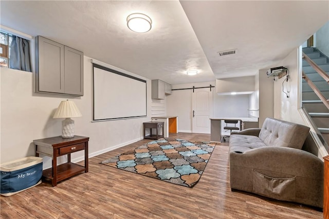 home theater room featuring wood finished floors, visible vents, baseboards, and a barn door