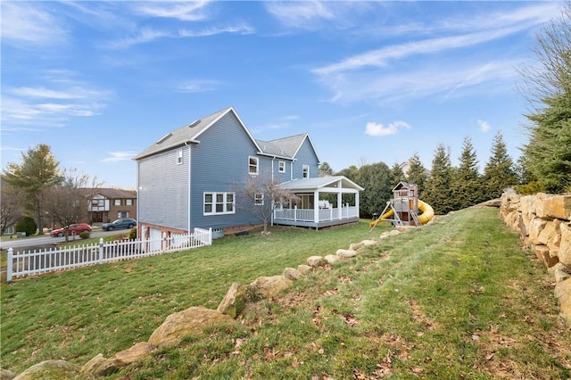 back of property with a yard, a playground, and fence