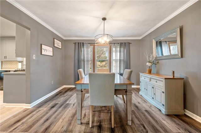 dining room with a chandelier, ornamental molding, baseboards, and wood finished floors