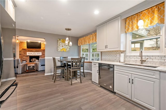 kitchen featuring light wood finished floors, stainless steel appliances, decorative backsplash, a brick fireplace, and a sink