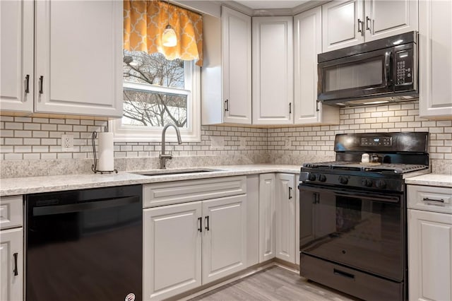 kitchen featuring a sink, white cabinetry, light wood-style floors, black appliances, and tasteful backsplash