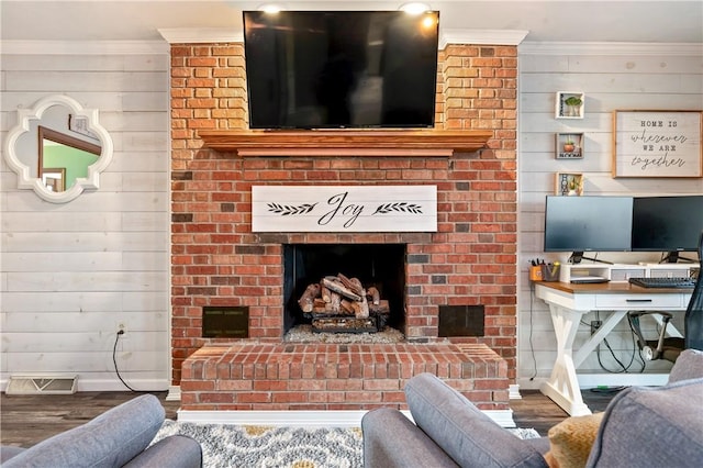 living room featuring a brick fireplace, visible vents, crown molding, and wood finished floors