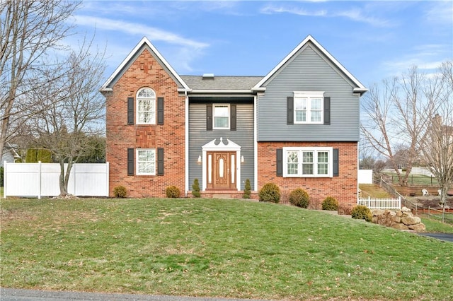 view of front of house with brick siding, a front lawn, and fence