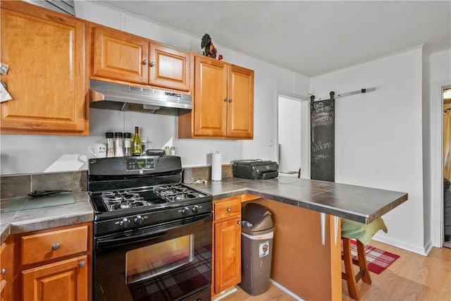 kitchen with a barn door, brown cabinetry, black range with gas stovetop, light wood-type flooring, and under cabinet range hood