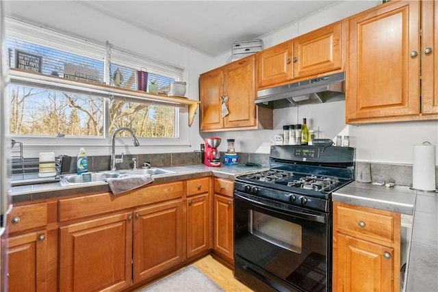 kitchen featuring gas stove, brown cabinets, a sink, and under cabinet range hood