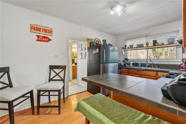 kitchen featuring brown cabinetry, a kitchen breakfast bar, freestanding refrigerator, light wood-type flooring, and a sink