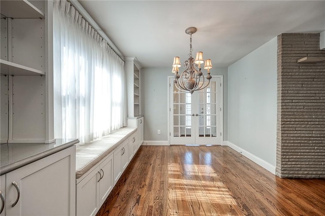 unfurnished dining area featuring french doors, a notable chandelier, baseboards, and wood finished floors