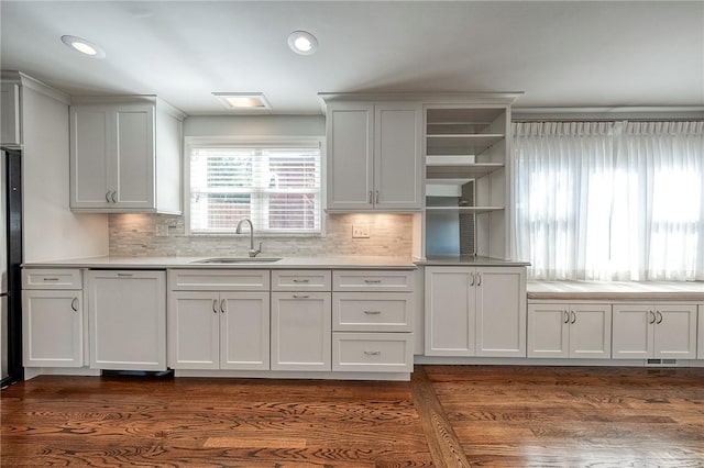 kitchen with dark wood finished floors, open shelves, light countertops, paneled dishwasher, and a sink