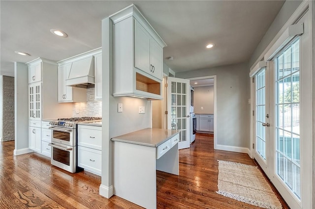 kitchen featuring dark wood-style flooring, baseboards, french doors, custom exhaust hood, and double oven range