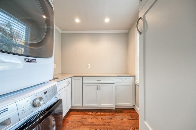 washroom with ornamental molding, stacked washer and dryer, dark wood-type flooring, and cabinet space