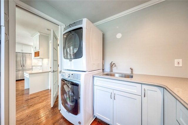 clothes washing area with cabinet space, ornamental molding, stacked washer / dryer, a sink, and wood finished floors