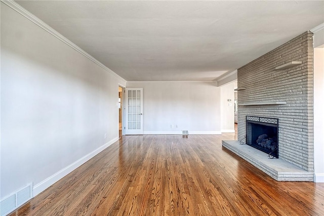 unfurnished living room featuring wood finished floors, visible vents, baseboards, ornamental molding, and a brick fireplace