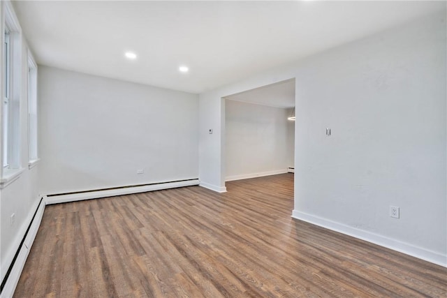 empty room featuring a baseboard radiator, baseboards, wood finished floors, and recessed lighting