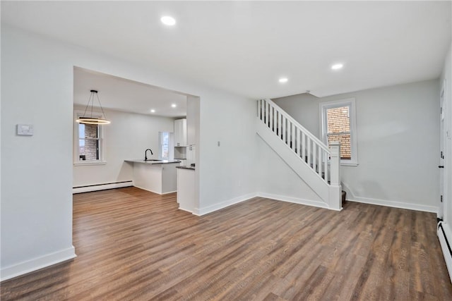 unfurnished living room featuring baseboards, stairway, dark wood-type flooring, baseboard heating, and a sink