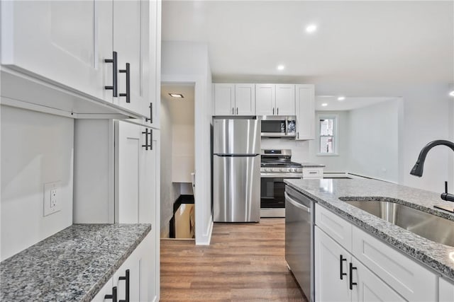 kitchen with light stone counters, light wood-style flooring, appliances with stainless steel finishes, white cabinetry, and a sink