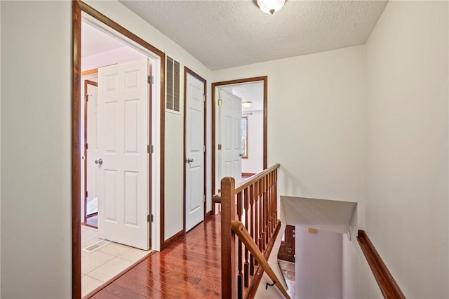 hall with visible vents, a textured ceiling, wood finished floors, and an upstairs landing