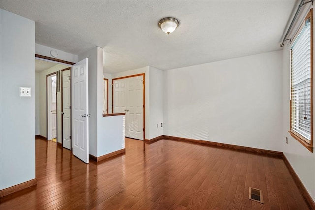 spare room featuring wood-type flooring, a textured ceiling, visible vents, and baseboards