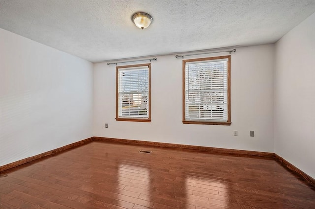 spare room featuring baseboards, visible vents, a textured ceiling, and hardwood / wood-style floors