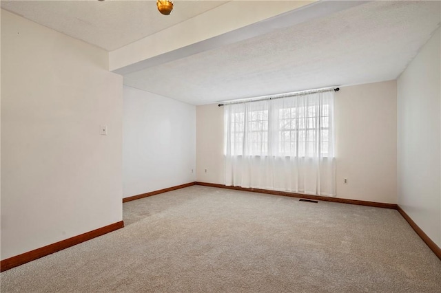 empty room with carpet, visible vents, a textured ceiling, and baseboards