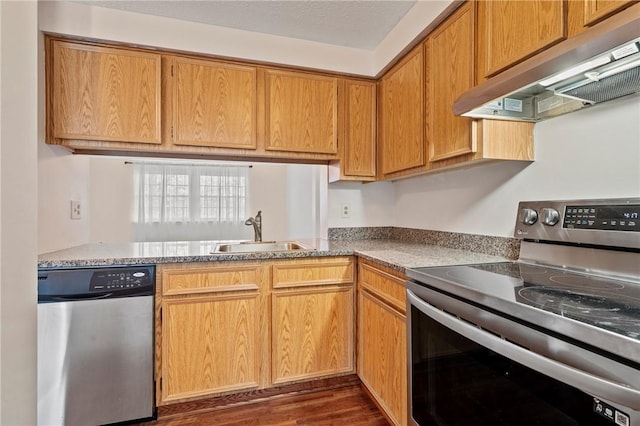 kitchen with dark wood finished floors, brown cabinetry, appliances with stainless steel finishes, under cabinet range hood, and a sink