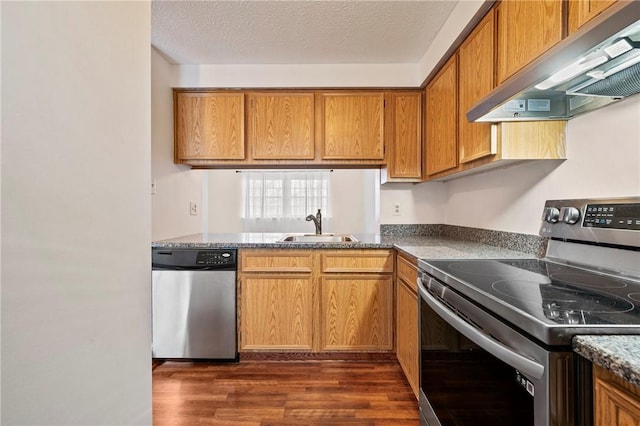 kitchen featuring wall chimney exhaust hood, appliances with stainless steel finishes, brown cabinets, dark wood-type flooring, and a sink