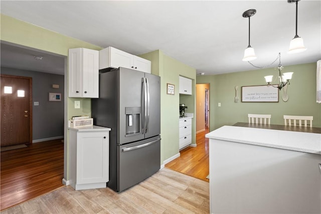 kitchen featuring white cabinets, hanging light fixtures, light wood-type flooring, stainless steel fridge with ice dispenser, and an inviting chandelier