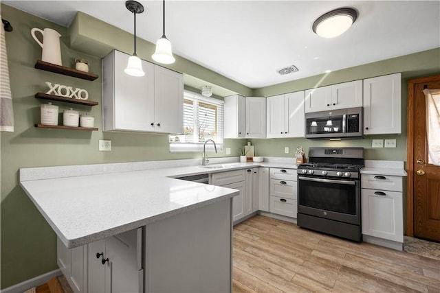 kitchen featuring light wood finished floors, white cabinets, appliances with stainless steel finishes, decorative light fixtures, and a peninsula