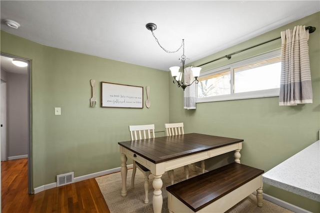 dining space featuring visible vents, a notable chandelier, baseboards, and wood finished floors