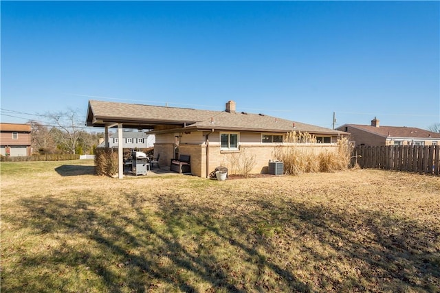 rear view of property with a chimney, fence, cooling unit, a yard, and brick siding