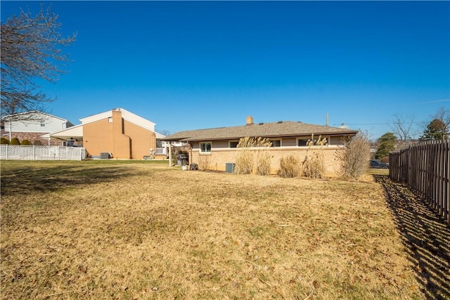 rear view of property with a chimney, fence, and a yard