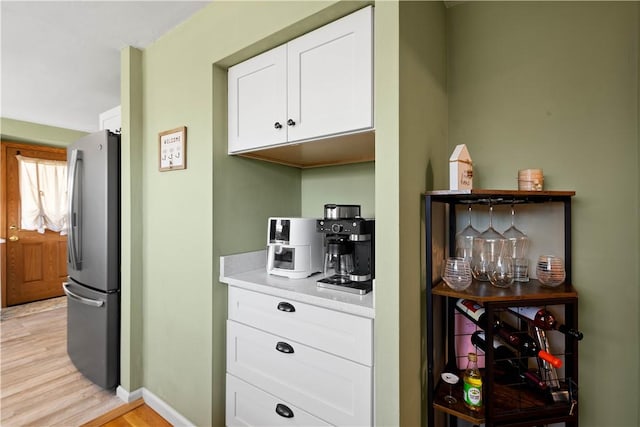 bar featuring light wood-style flooring, freestanding refrigerator, and baseboards