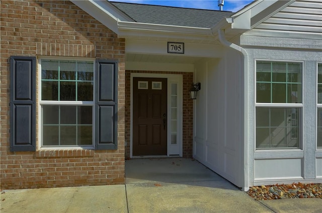 view of exterior entry featuring brick siding and a shingled roof