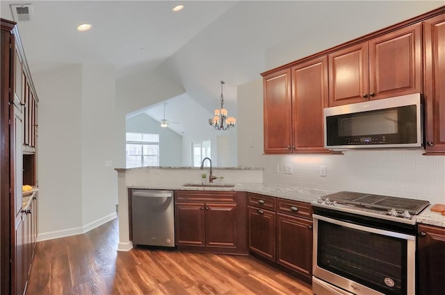 kitchen featuring a peninsula, light stone countertops, appliances with stainless steel finishes, and a sink