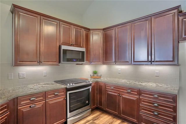 kitchen featuring tasteful backsplash, vaulted ceiling, light stone counters, light wood-style flooring, and stainless steel appliances