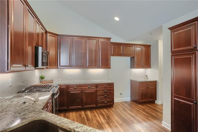 kitchen featuring tasteful backsplash, appliances with stainless steel finishes, light wood finished floors, light stone countertops, and vaulted ceiling