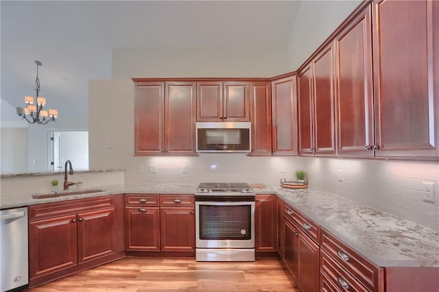 kitchen featuring light wood finished floors, light stone counters, appliances with stainless steel finishes, and a sink