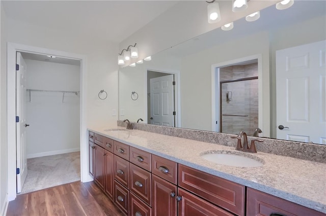 bathroom featuring a walk in closet, a stall shower, a sink, wood finished floors, and double vanity