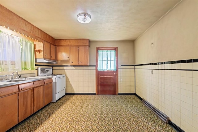 kitchen featuring a sink, tile walls, light countertops, white gas range oven, and brown cabinets