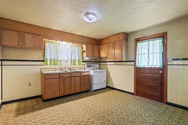 kitchen with under cabinet range hood, tile walls, range, and a sink