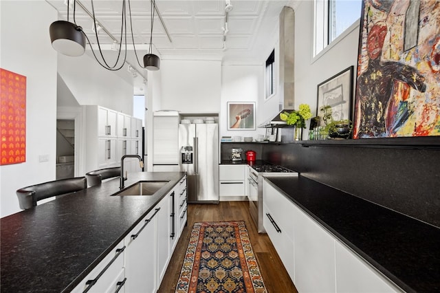 kitchen featuring stainless steel appliances, wall chimney exhaust hood, dark countertops, and a sink