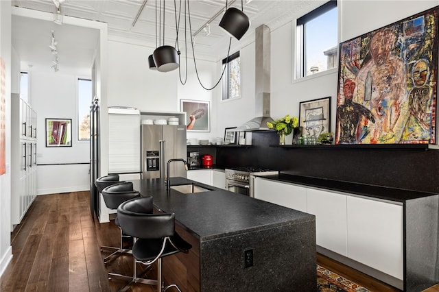 kitchen featuring dark wood-style floors, high end appliances, dark countertops, a sink, and wall chimney range hood