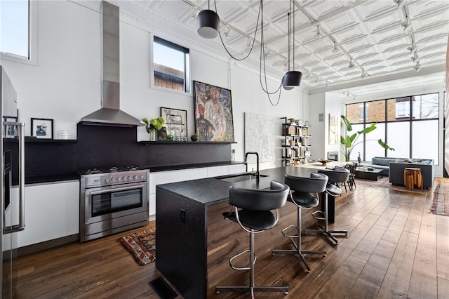 kitchen with an ornate ceiling, stainless steel range with gas cooktop, dark countertops, a sink, and wall chimney range hood