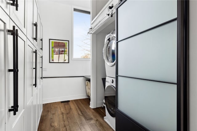 clothes washing area with stacked washer / drying machine, laundry area, baseboards, and dark wood-style flooring