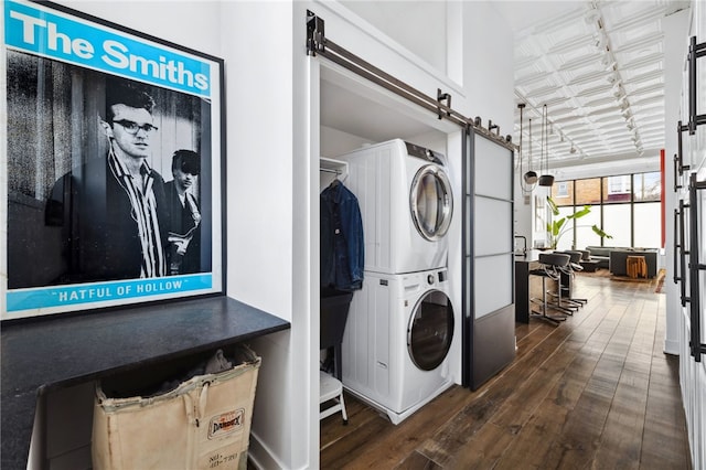 clothes washing area with a barn door, stacked washer and dryer, dark wood-type flooring, laundry area, and an ornate ceiling