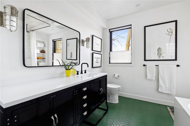 bathroom with baseboards, plenty of natural light, vanity, and toilet