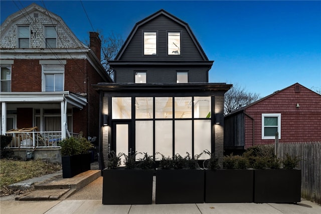 back of property with covered porch, brick siding, and a gambrel roof