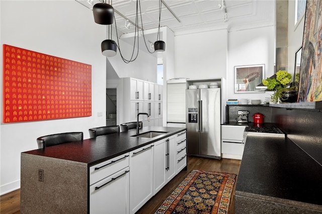 kitchen with a sink, white cabinetry, high end fridge, dark wood-style floors, and dark countertops