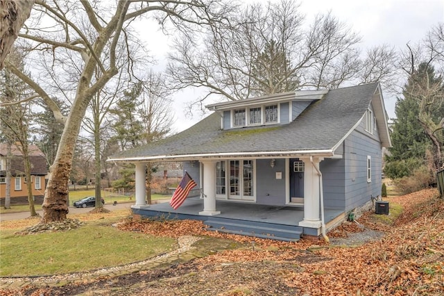 view of front of home with covered porch, roof with shingles, a front yard, and cooling unit